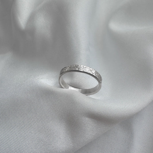 Silver ring with sand texture on a light gray fabric background