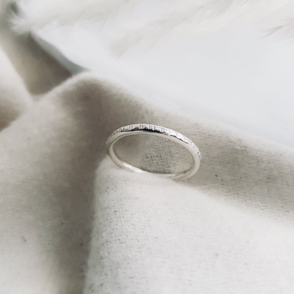 a silver ring textured with hammered lines on cream fabric