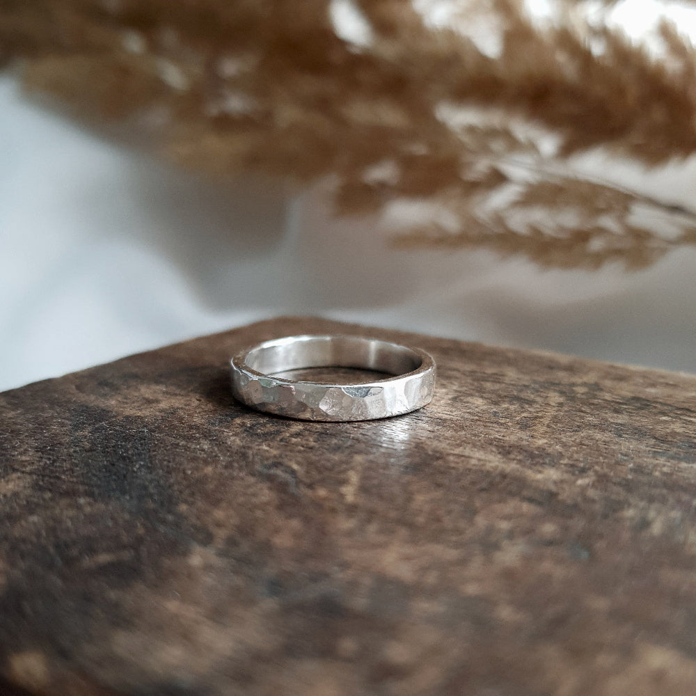 a 3mm wide silver hammered ring on wood with leafs in the background