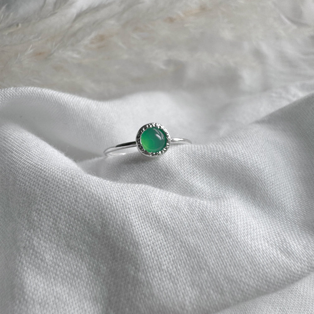 A Silver ring with a 5mm Green Crystaphase stone in a rustic setting on white fabric background