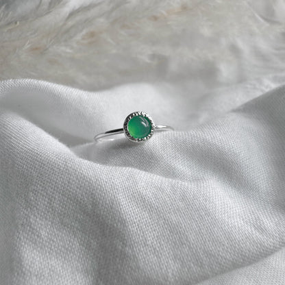 A Silver ring with a 5mm Green Crystaphase stone in a rustic setting on white fabric background