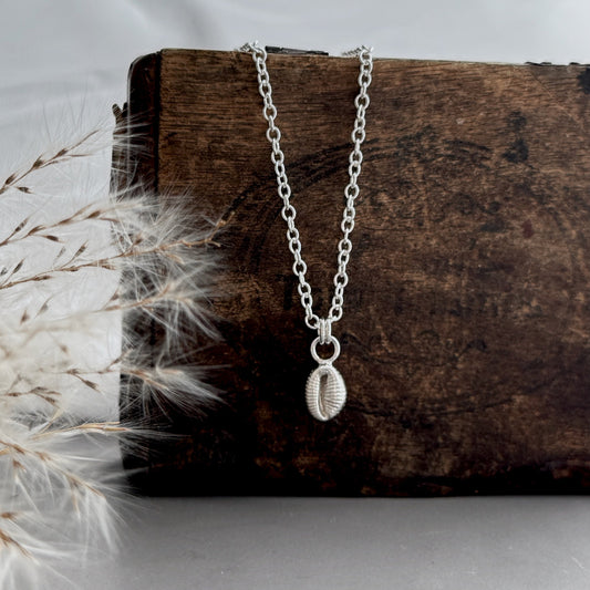 Silver Groatie Buckie necklace/pendant on a wooden block with dried grass at the edge of the picture