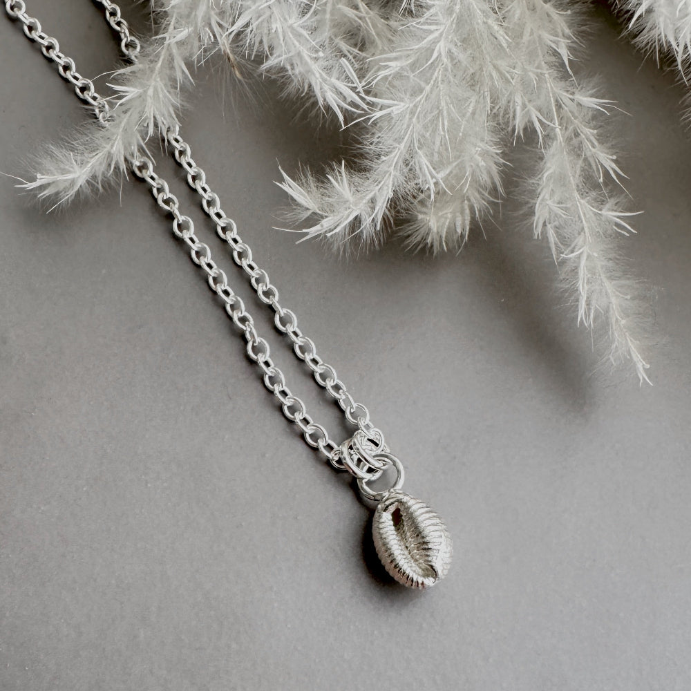 Silver necklace with a Groatie Buckie shell pendant on a grey surface with white dried grasses