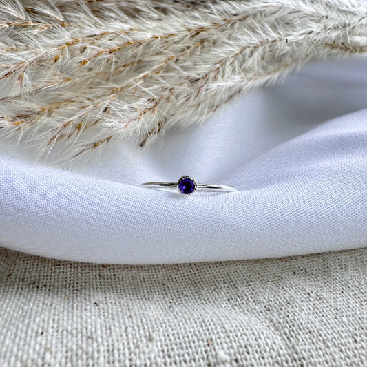 A silver ring with a blue/purple Iolite stone, placed on a white fabric surface.