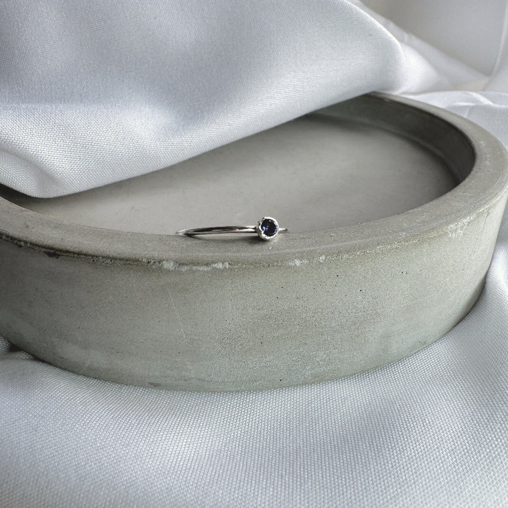 A silver ring with a blue/purple Iolite stone, resting on the edge of a grey dish