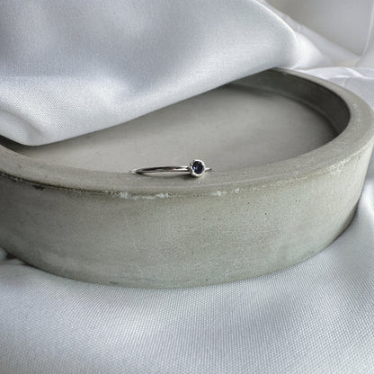 A silver ring with a blue/purple Iolite stone, resting on the edge of a grey dish
