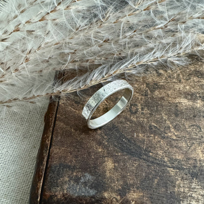 Silver textured ring on a textured wooden surface with dried grasses