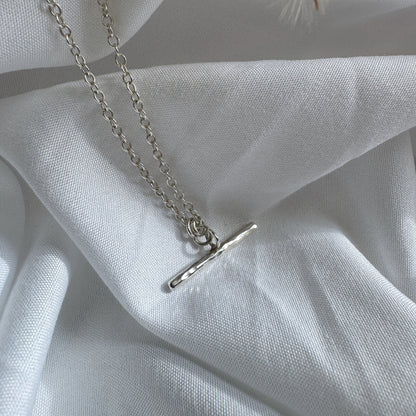 Silver t-bar necklace with a simple pendant on a white fabric background