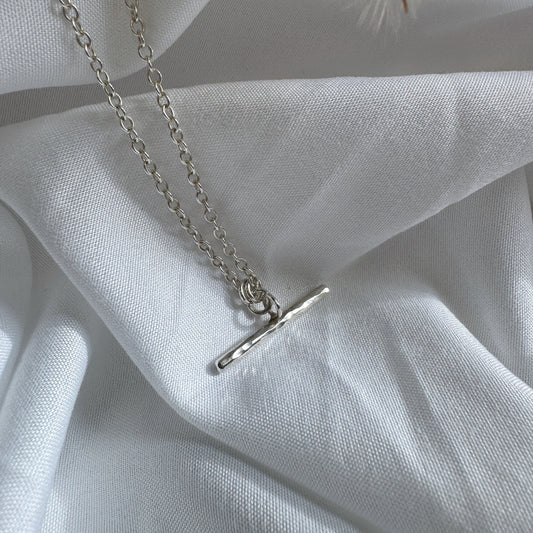 Silver t-bar necklace with a simple pendant on a white fabric background