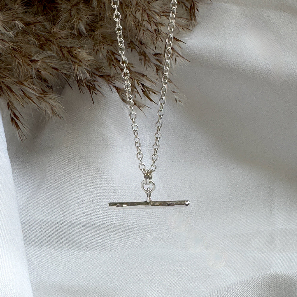 Silver t-bar necklace with a simple pendant on a white fabric background