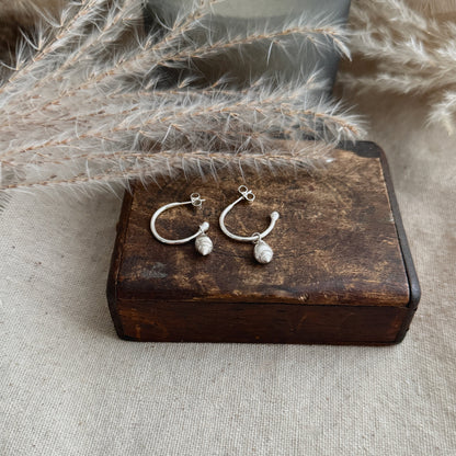 Pair of silver hoop earrings on a wooden box with dried plants in the background
