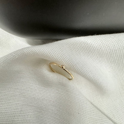 A 9ct gold ball stacking ring with a small ball on top, placed on a white textured surface.