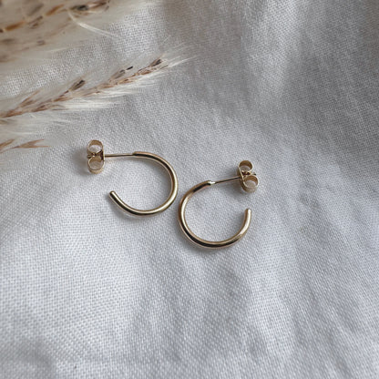 A pair of 9ct gold hoop earrings placed on a white fabric surface.