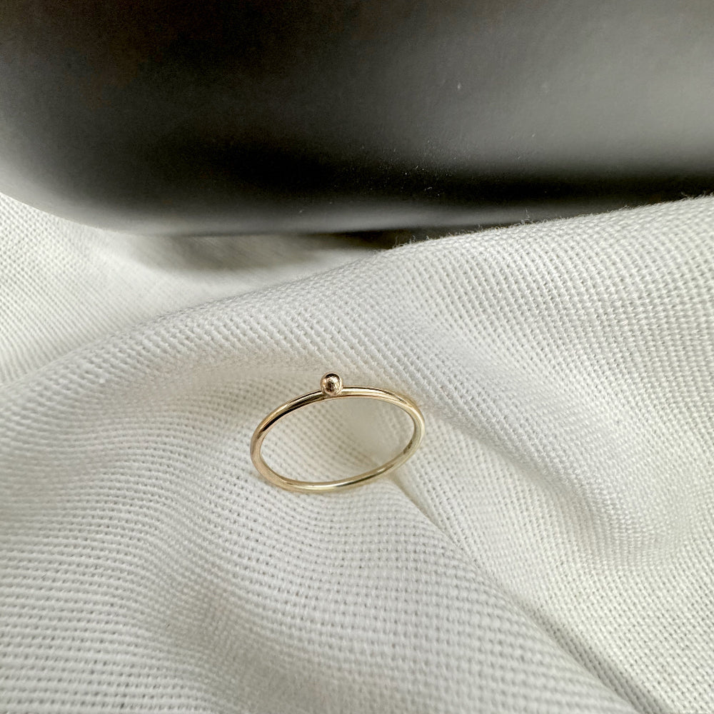 A 9ct gold ball stacking ring with a small ball on top, placed on a white textured surface.