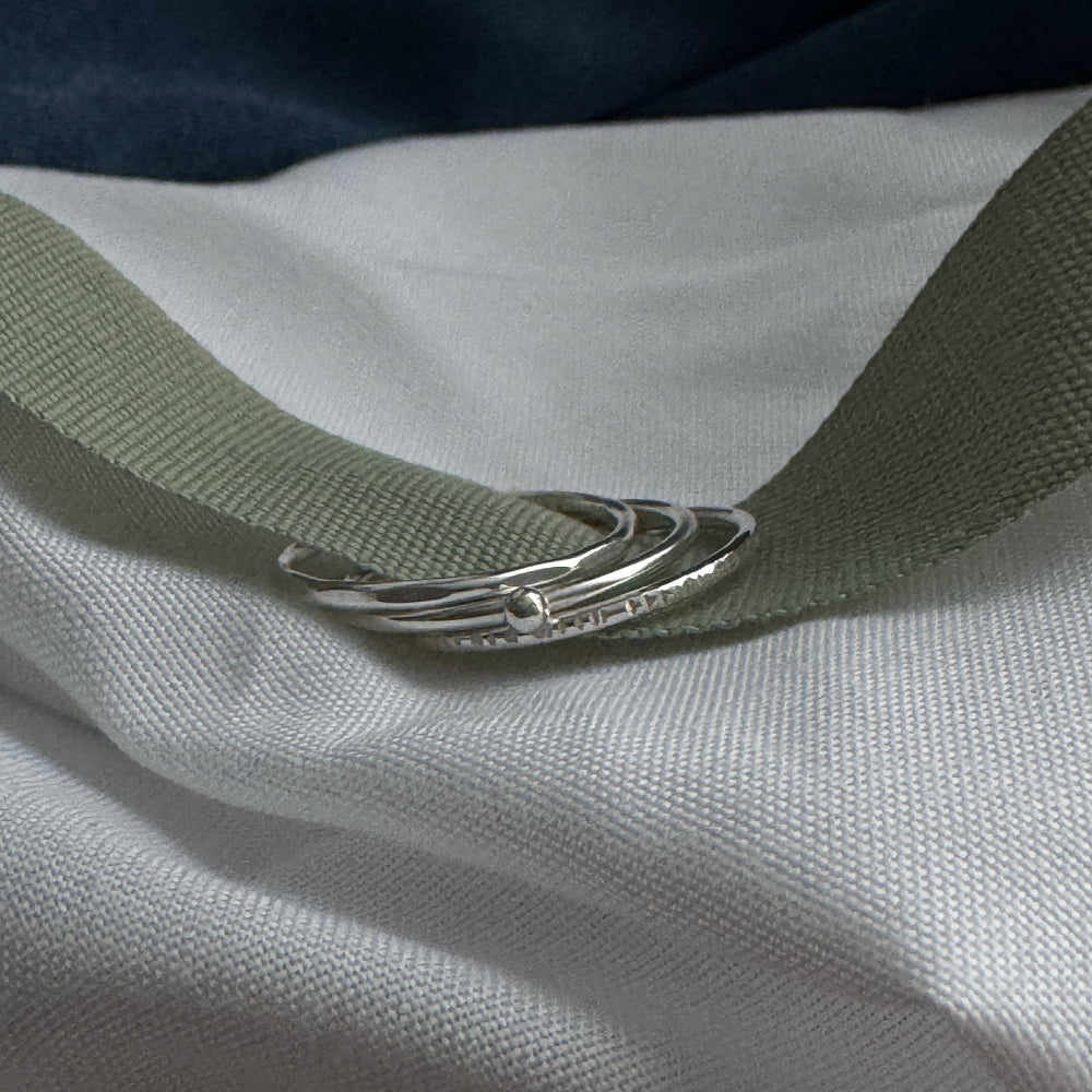 Close-up of a green ribbon with 3 silver stacking rings on a white fabric background