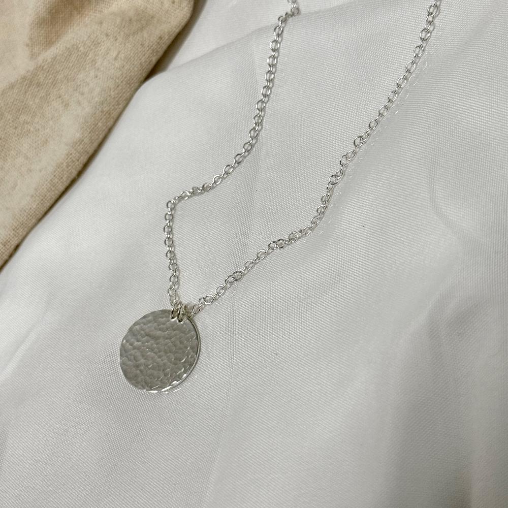 Hammered Silver circle pendant on chain on a white fabric bacground