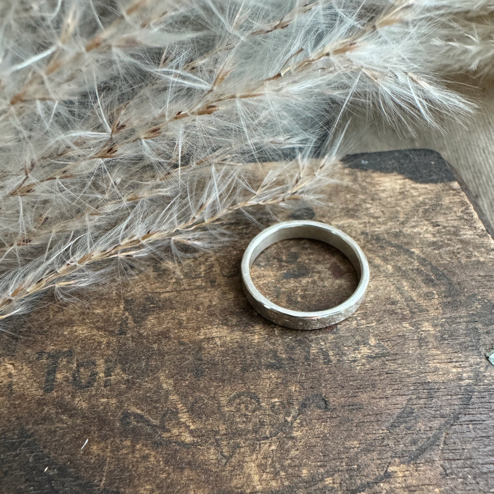 Silver ring on a wooden surface with dried plants in the background
