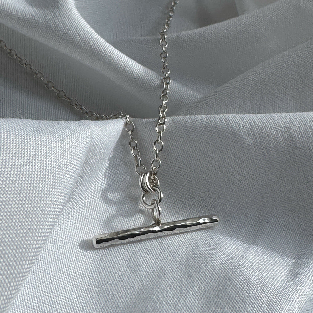 Silver necklace with a bar pendant on a light gray fabric background