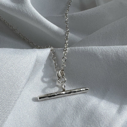 Silver necklace with a bar pendant on a light gray fabric background
