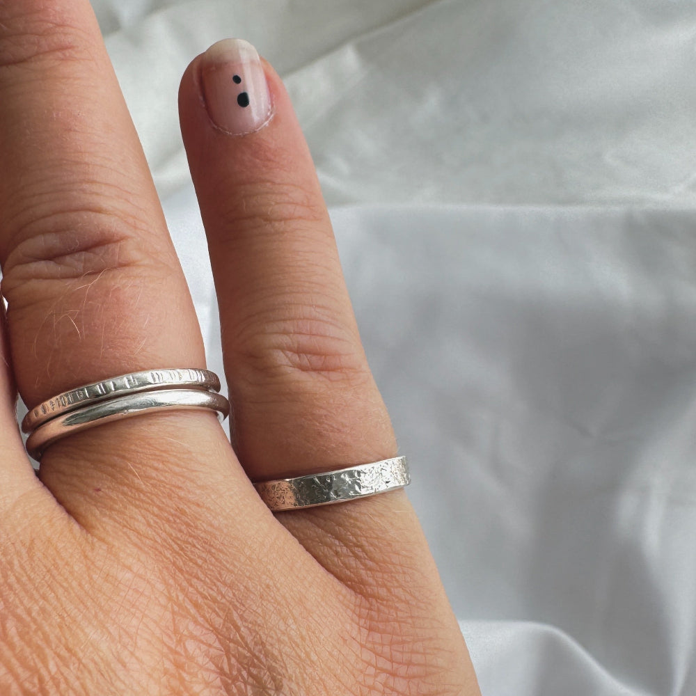 Hand wearing two silver rings on fourth fing and one on little finger on a white fabric background