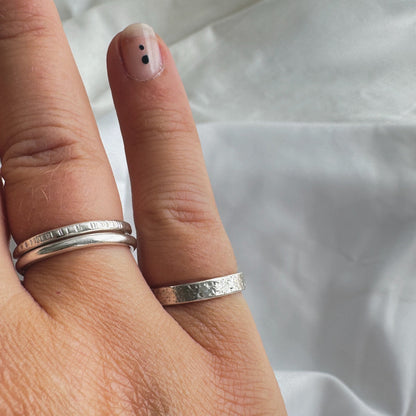 Hand wearing two silver rings on fourth fing and one on little finger on a white fabric background