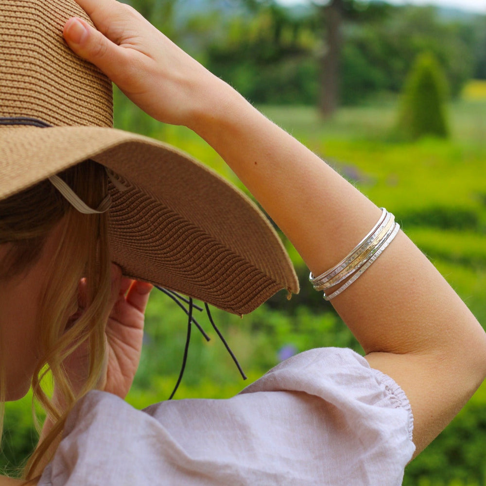 a model wearing a stack of 5 bangles  she has her arm up touching her straw hat