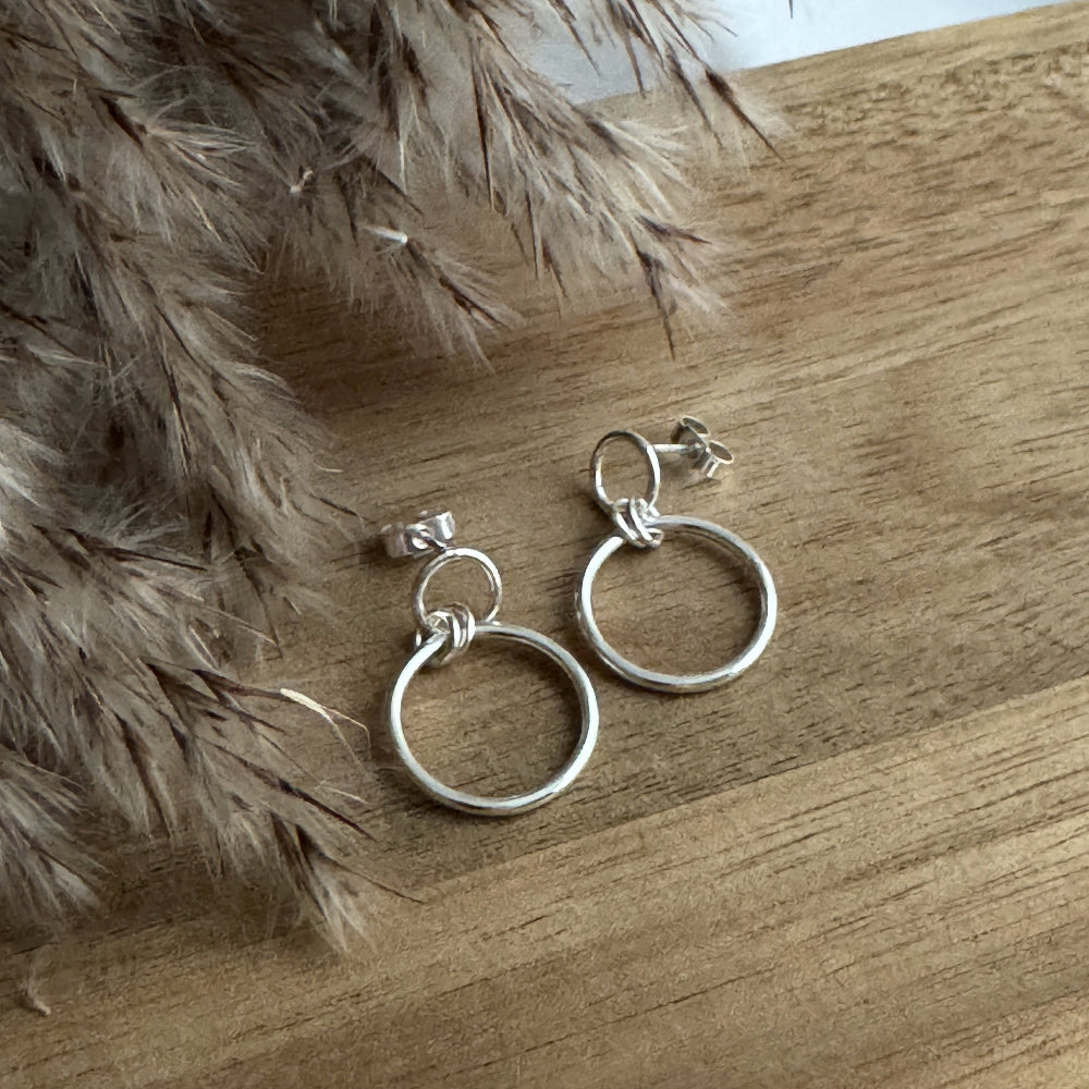 Silver hoop earrings on a wooden surface with a fluffy beige background
