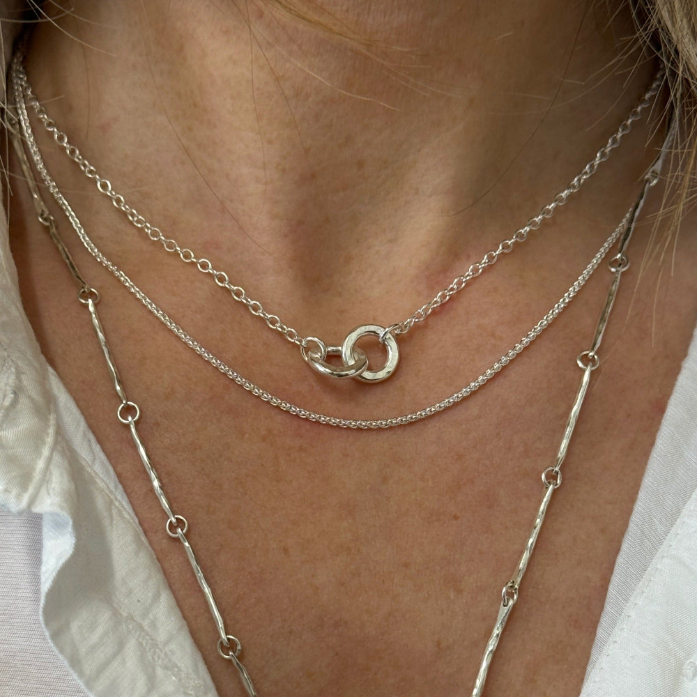 Lady wearing 3 necklaces layered together the first is 2 hammered silver links interlocked on a silver chain, the 2nd is a fine silver chain and the 3rd is a longer hammered chain