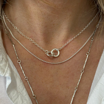 Lady wearing 3 necklaces layered together the first is 2 hammered silver links interlocked on a silver chain, the 2nd is a fine silver chain and the 3rd is a longer hammered chain