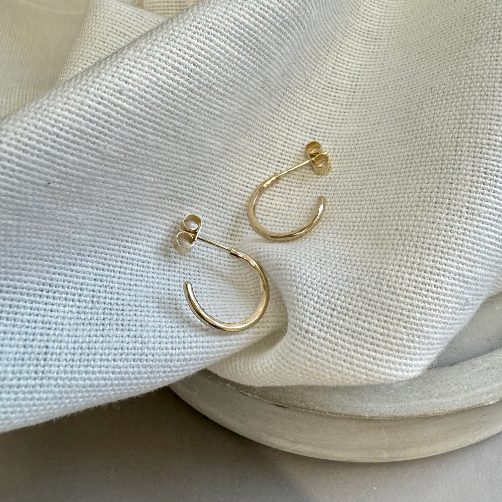 A pair of small hammered 9ct gold hoop earrings placed on a cream textured fabric