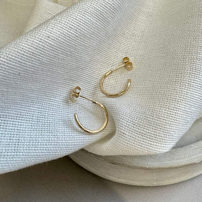 A pair of small hammered 9ct gold hoop earrings placed on a cream textured fabric