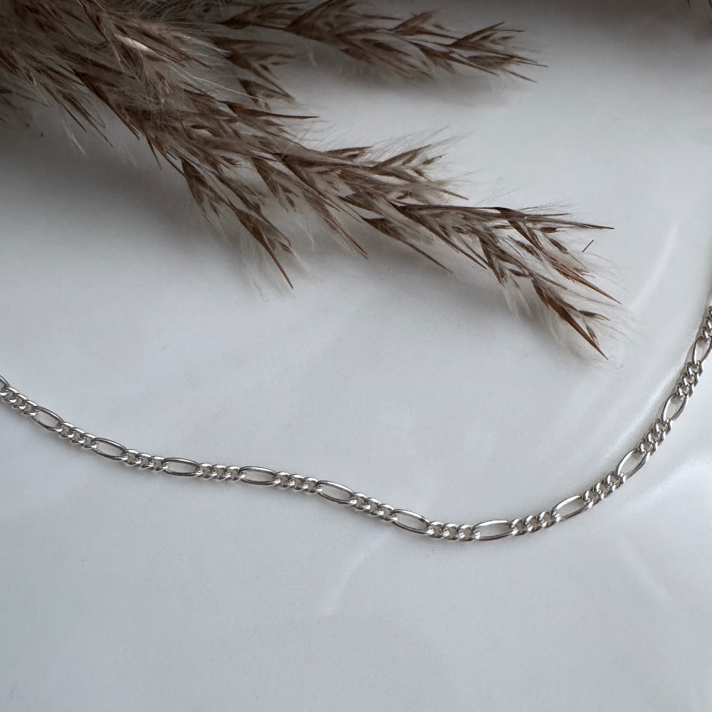 Silver figaro chain bracelet on a light background with dried grasses
