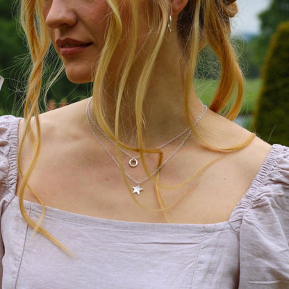 a female wearing a lilac top and wearing two silver necklace the shortest is a small silver hammered circular pendant, and the slightly long one is a silver star pendant