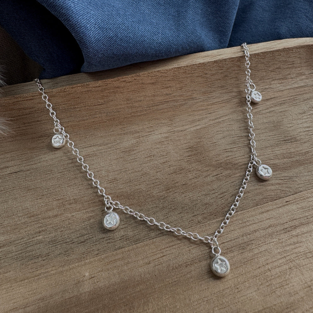 Silver necklace with small round pendants on a wooden surface with a blue fabric background