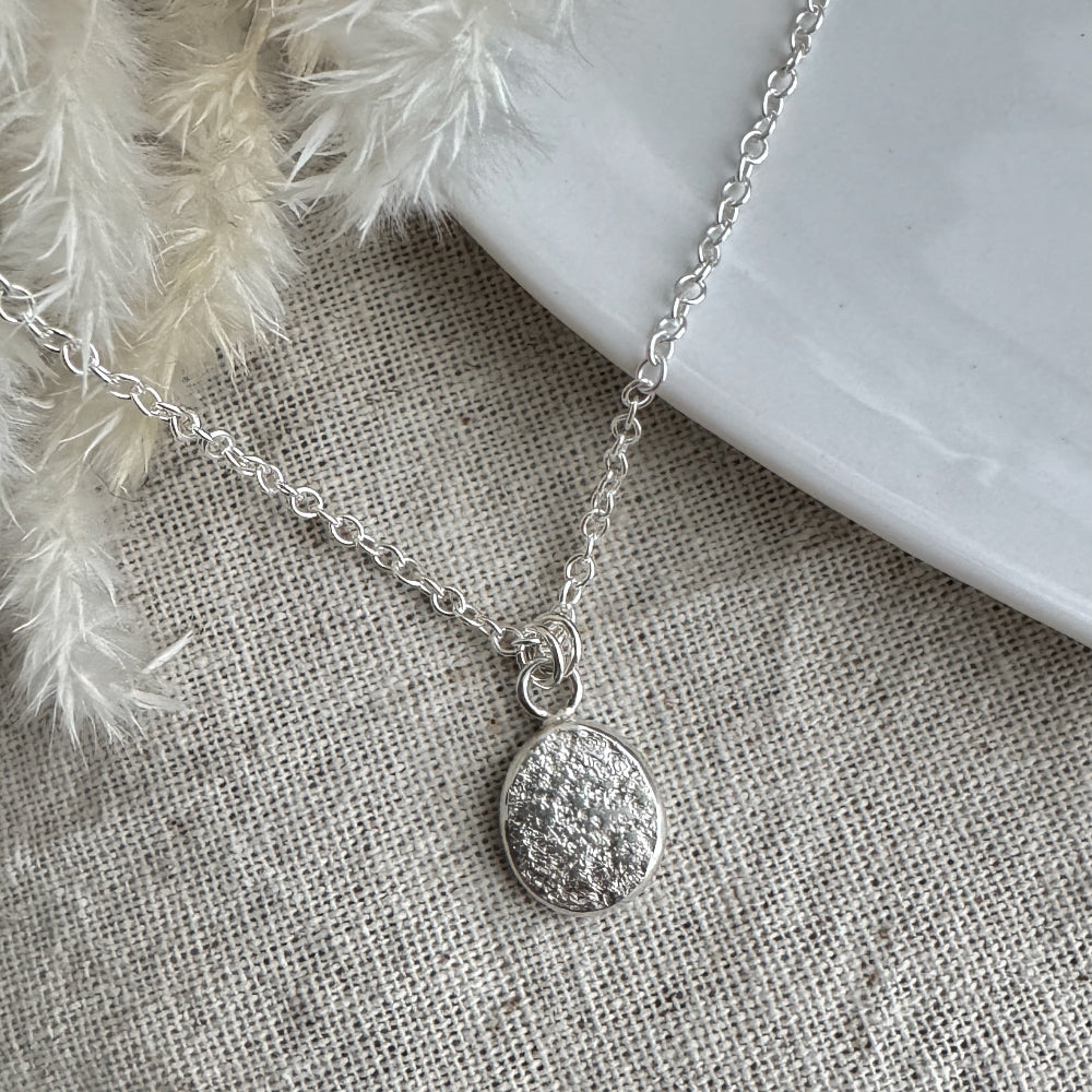 Silver necklace with a pendant on a textured fabric surface