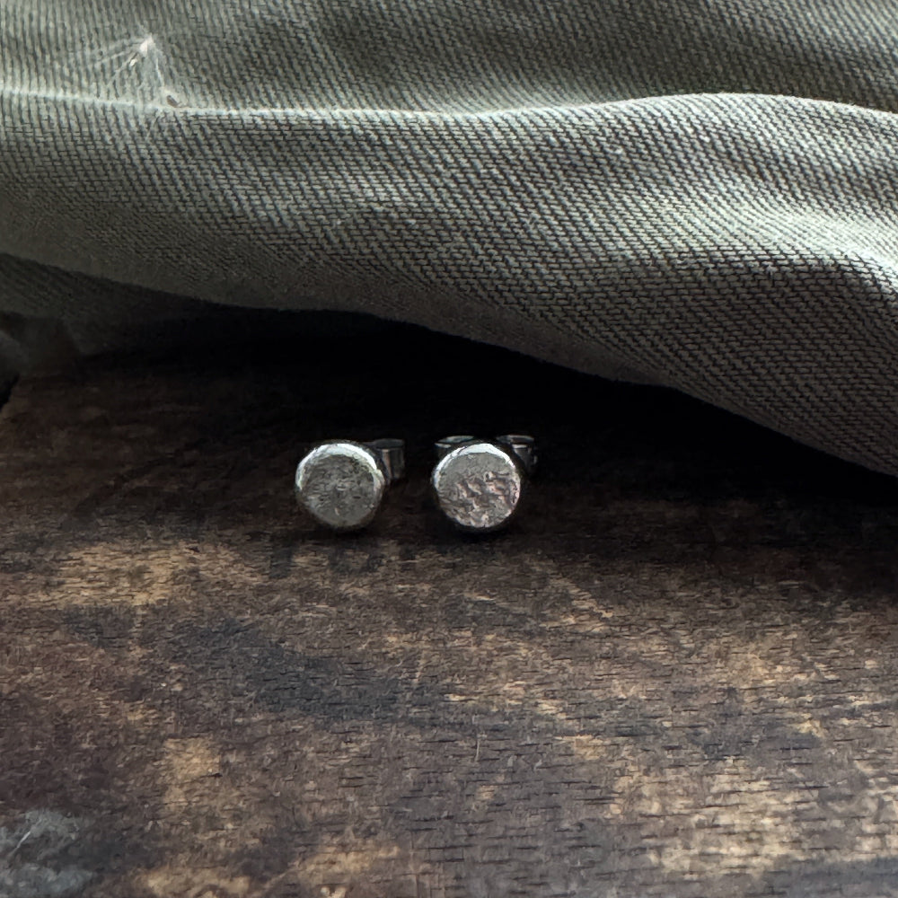 Round silver earrings on a wooden surface with a gray fabric background