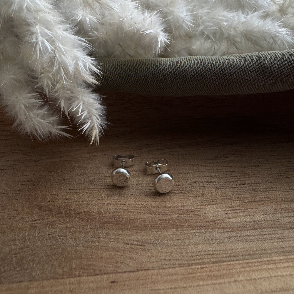 Silver stud earrings on a wooden surface with a fluffy white rug in the background