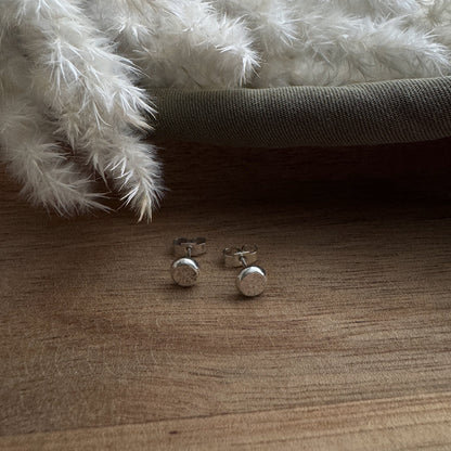 Silver stud earrings on a wooden surface with a fluffy white rug in the background