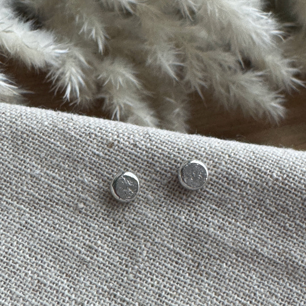 Silver stud earrings on a textured fabric surface