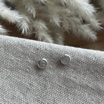Silver stud earrings on a textured fabric surface