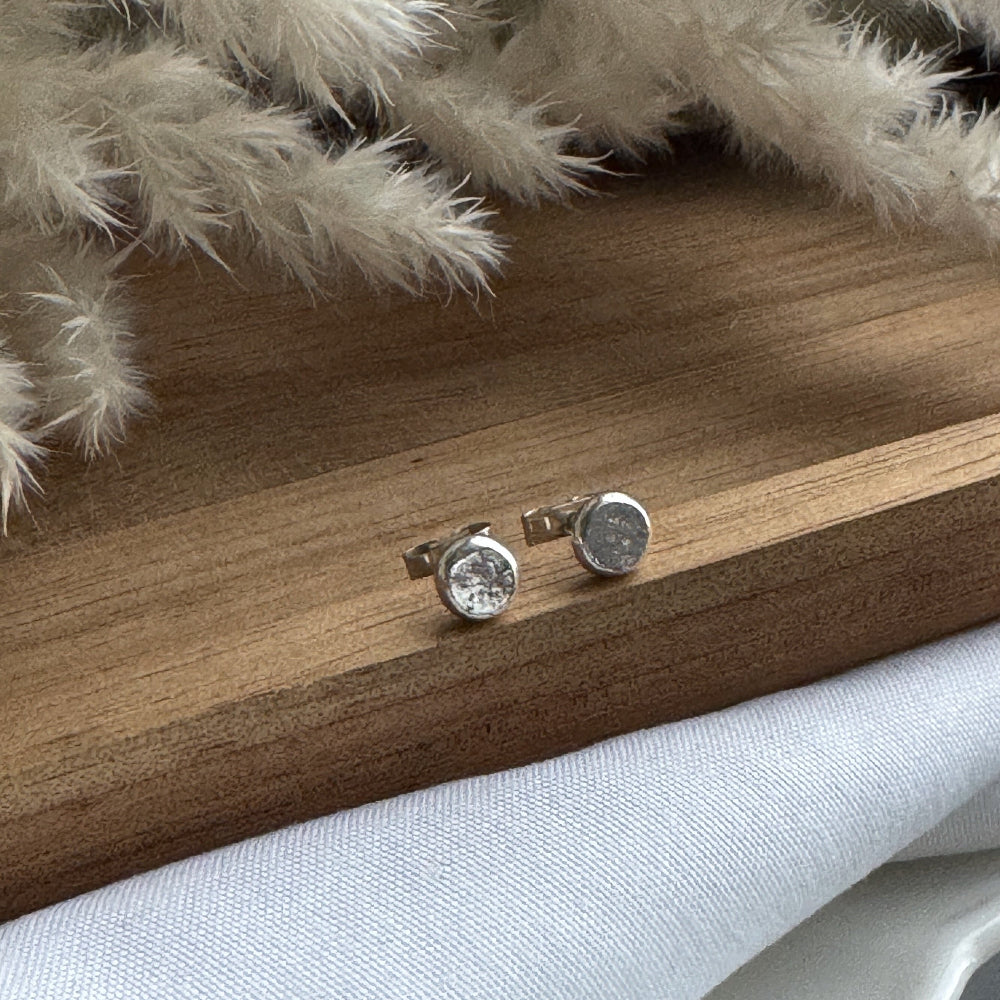 Silver stud earrings on a wooden surface with decorative white branches.