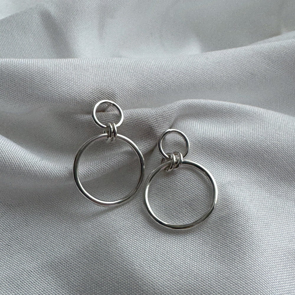Pair of silver hoop earrings on a light gray fabric background