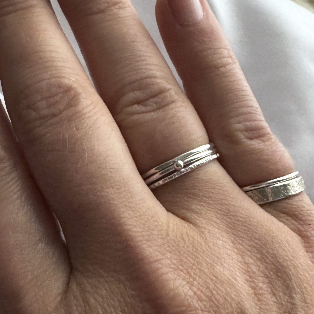 Close-up of a hand wearing the silver rings on the fourth finger and two on the little finger on a neutral background