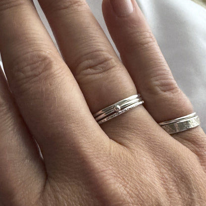 Close-up of a hand wearing the silver rings on the fourth finger and two on the little finger on a neutral background