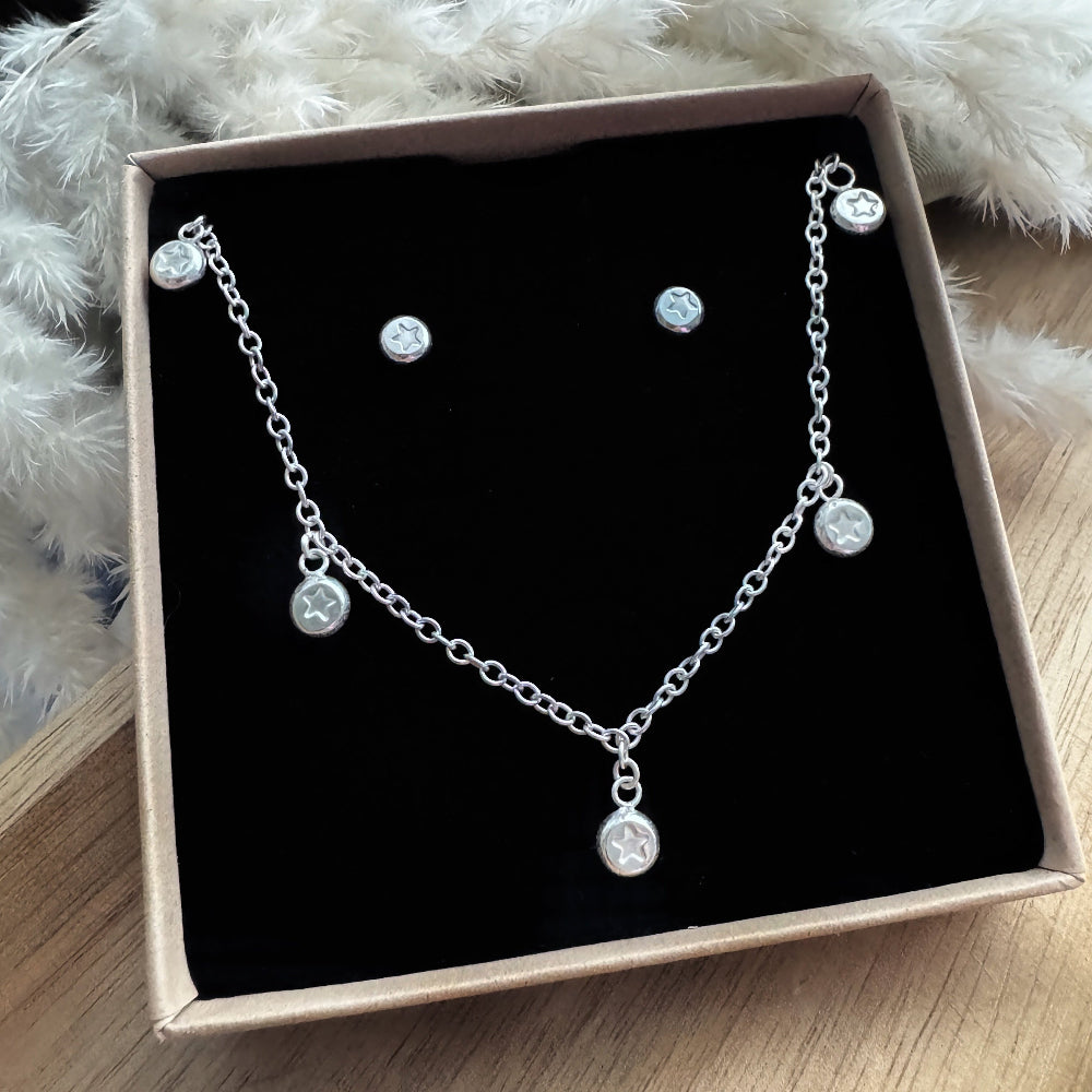 Silver necklace and earrings set in a box on a wooden surface with a fluffy white foliage in the background.