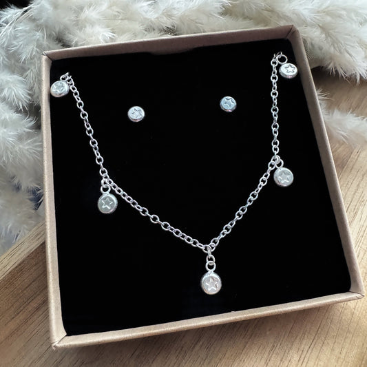 Silver necklace and earrings set in a box on a wooden surface with a fluffy white foliage in the background.