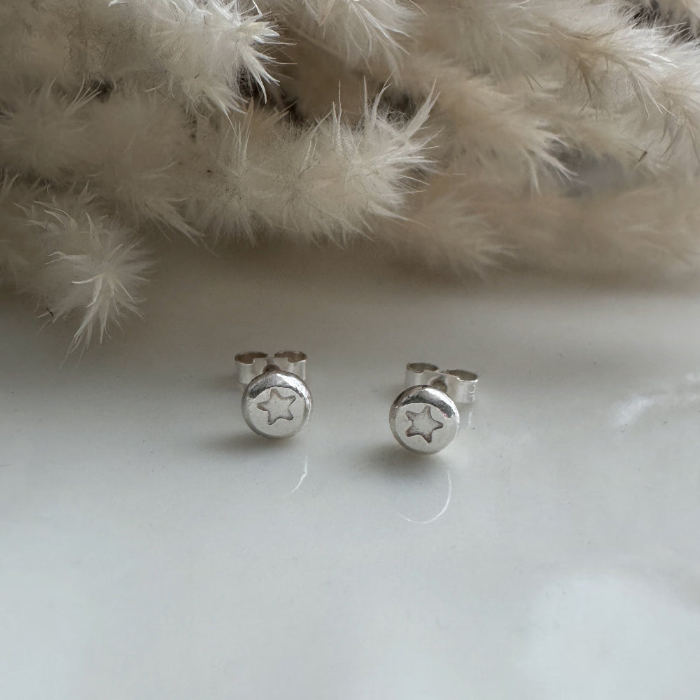 Silver star earrings on a white surface with a fluffy white background