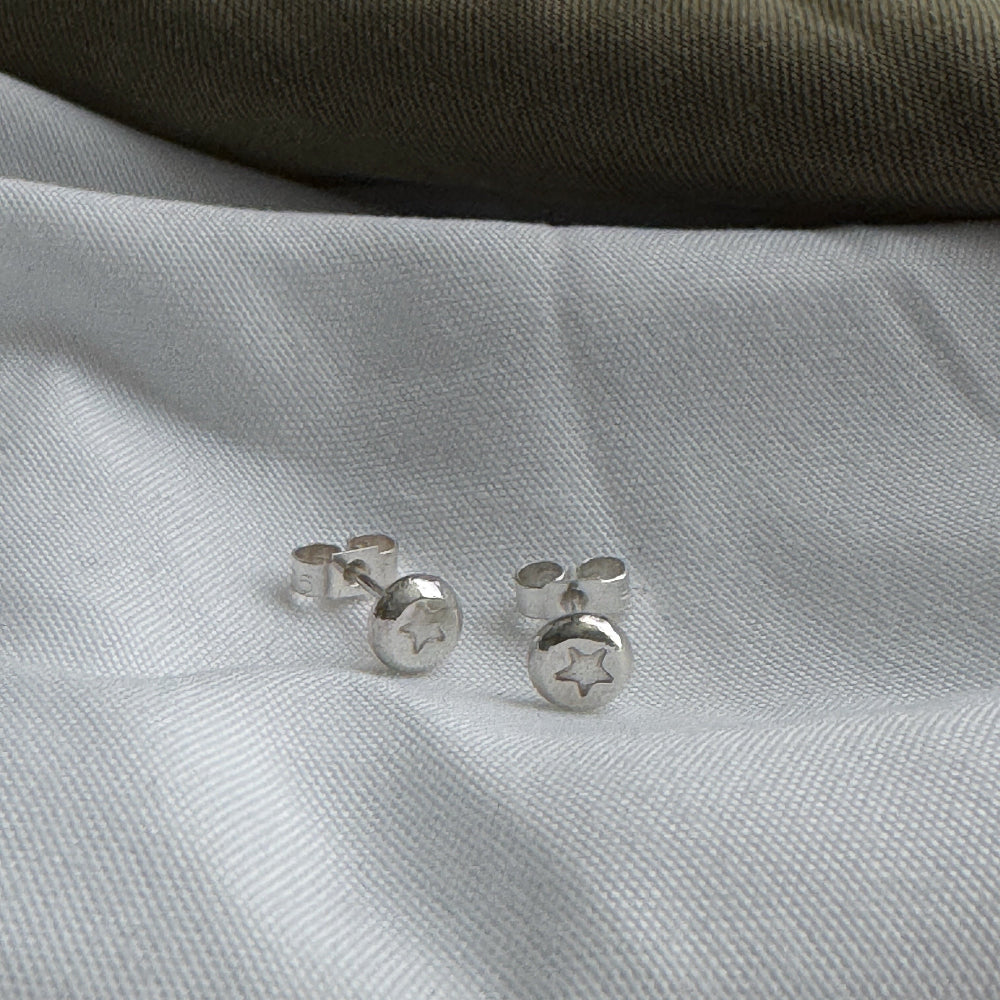 Silver stud earrings with a star stamped into them on a white fabric background