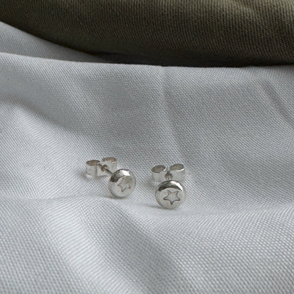 Silver stud earrings with a star stamped into them on a white fabric background