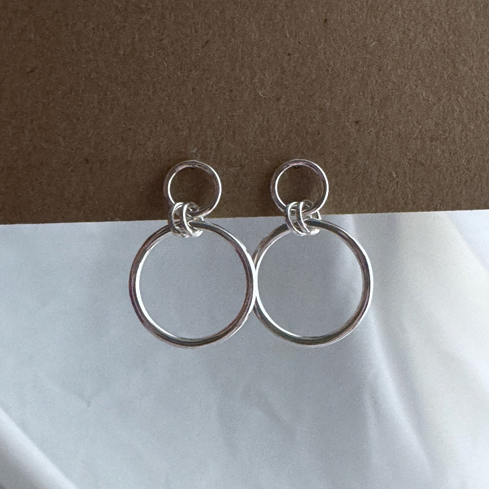 Silver hoop earrings on a white surface with a brown background